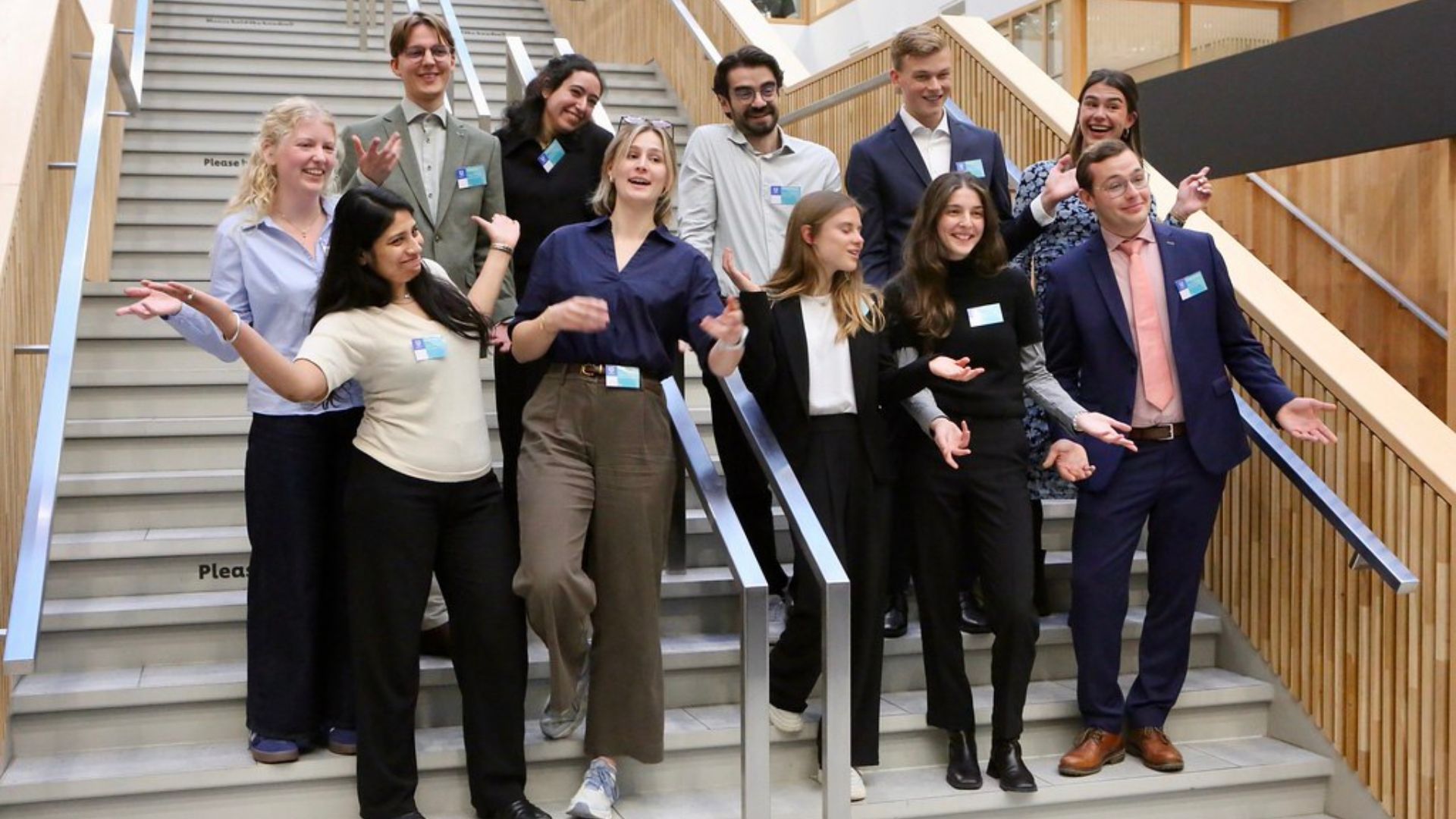 Group of eleven people posing on a staircase, smiling and gesturing happily.
