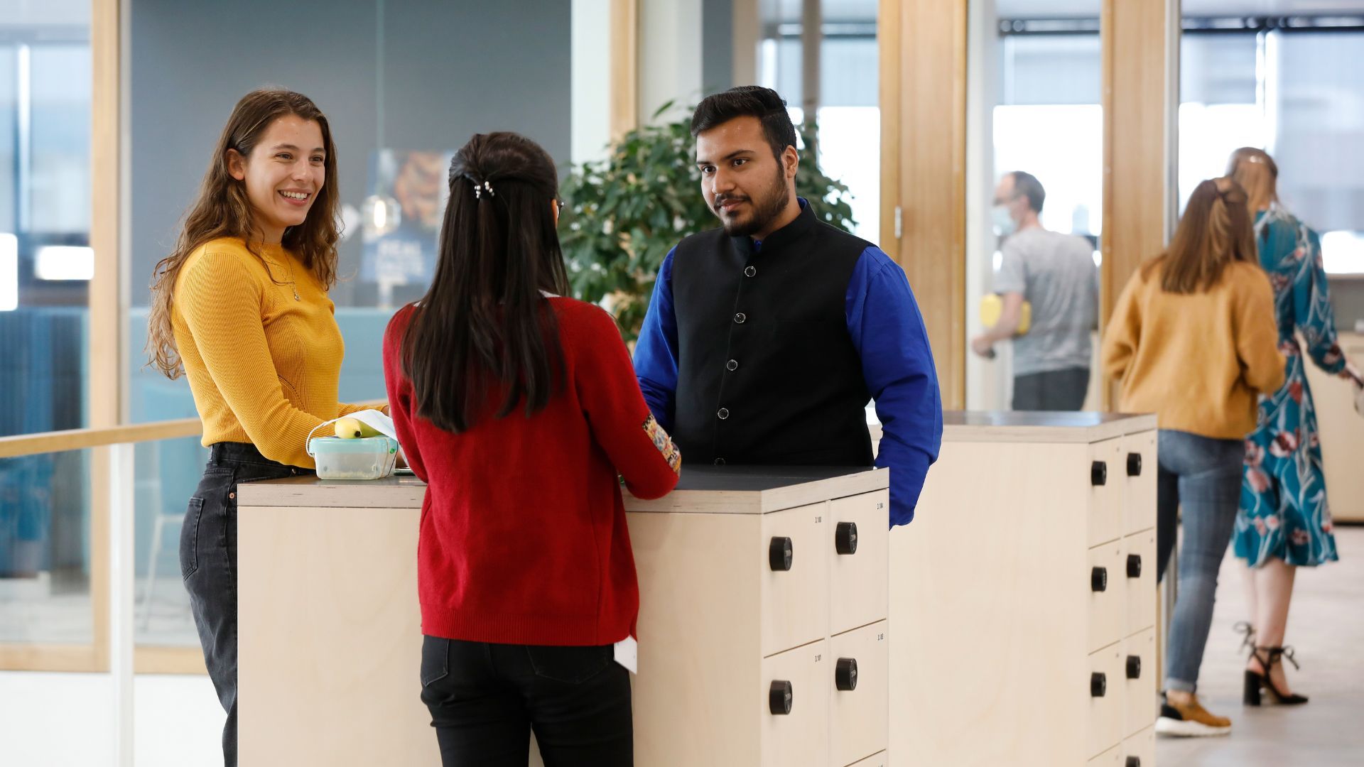 Three people talking near lockers in an office space.