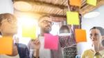 Three people organize Post-it notes on a window.