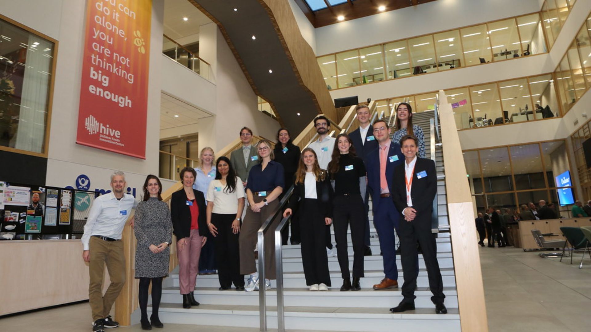 Group of people standing on stairs inside a modern building with a red banner.