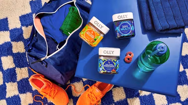 A flatlay image of OLLY vitamins and supplements. Nearby a water bottle and orange training shoes are pictured.