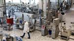 A man in a white coat and white cap walking in a food factory.