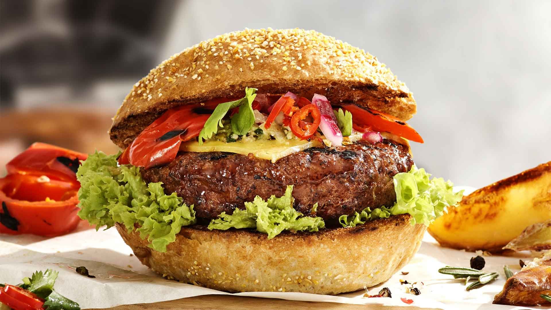 Image of a raw burger in a bun with tomatoes and vegetables