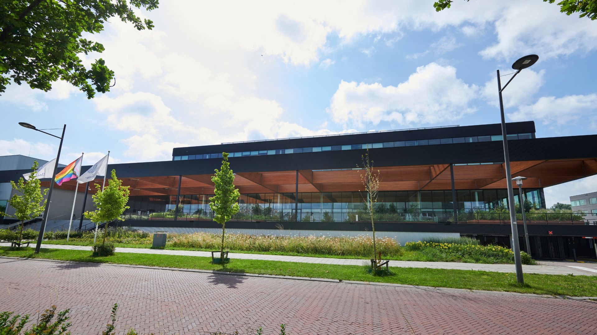 Modern building with glass facade and three flags in front.